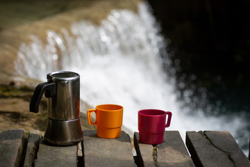 Two cup of coffee and jar on a waterfall stream background