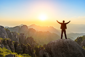 Hiker is standing on a rock with raised hands and enjoying sunrise