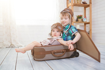 Little boy and girl in suitcase in the form of an aircraft pilot and traveler playing in room