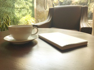 Afternoon tea in white cup with notebook on brown wooden table in the cafe.