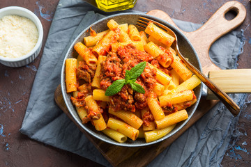 Delicious rigatoni pasta with italian tomato meat ragu sauce served in a pan on dark brown background. Traditional pasta dish concept. Home made lunch