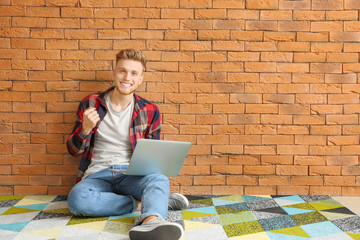 Wall Mural - Happy young man with laptop sitting near brick wall