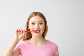 Wall Mural - Beautiful woman cleaning teeth on light background