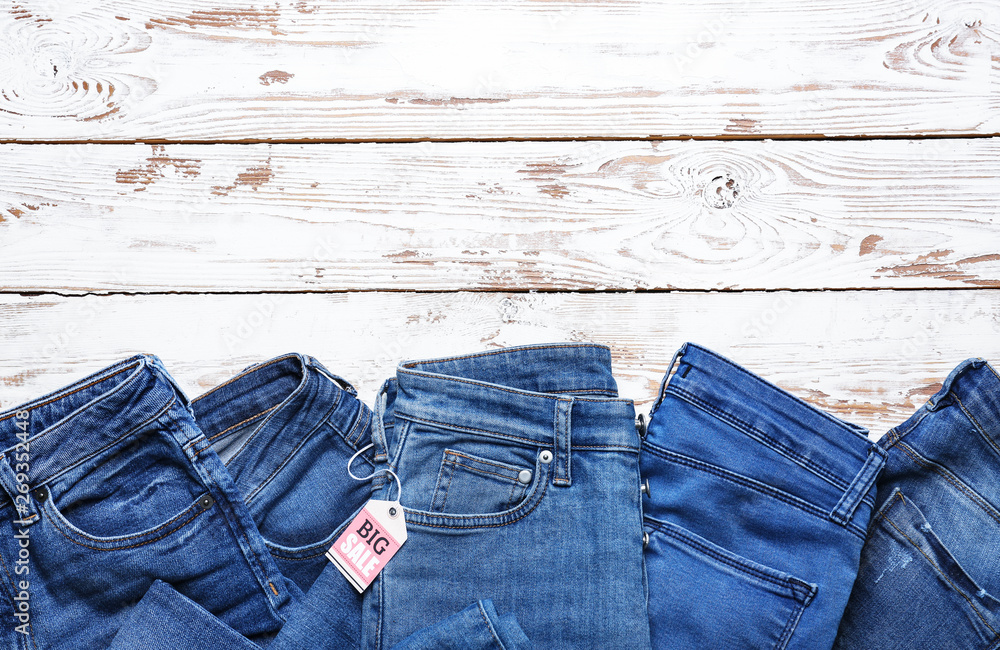Different jeans pants with shopping tag on white wooden background