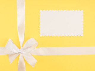 Wall Mural - Bow from white satin ribbon on yellow background with copy space