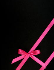 Wall Mural - Bow from pink satin ribbon diagonally on black background