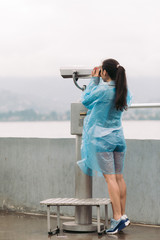 Wall Mural - female tourist looking through coin operated binoculars with sea view in rainy weather