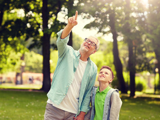 Wall Mural - family, generation, communication and people concept - happy grandfather and grandson walking and pointing fingers up at summer park