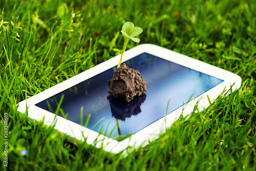 a touch screen of smartphone,tablet,cell phone with seedling growing up on screen over green grass. abstract background to green communication technology concept.