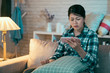upset asian korean wife viewing online content in smart phone sitting on sofa in dark living room at home at night. sad girl binge watching love film romantic miserable movie on cellphone frowning.