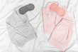 Two warm pajamas on bed, male and female, sleep masks. Gray and pink nightwear on white sheet. Top view. Flat lay.