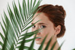 Young redhead woman posing isolated over white wall background with leaf green flowers.