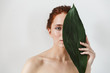 © Drobot Dean - Young redhead woman posing isolated over white wall background with leaf green flowers.