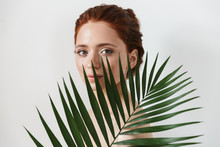 Young Redhead Woman Posing Isolated Over White Wall Background With Leaf Green Flowers.
