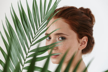 Wall Mural - young redhead woman posing isolated over white wall background with leaf green flowers.