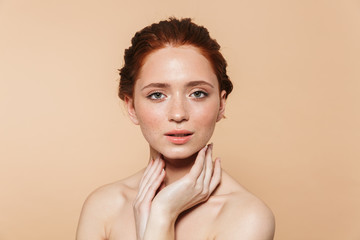 Wall Mural - Young redhead woman posing isolated over beige wall background.