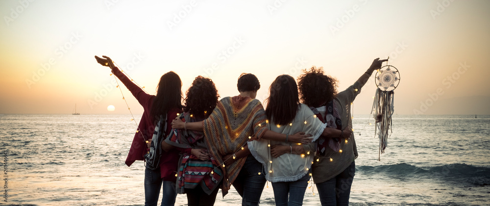 Romance and emotion concept with group of people women friends viewed from back hugging and ejoying the sunset in outdoor nature sea vacation concept - friendship and freedom for travelers - obrazy, fototapety, plakaty 