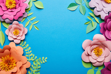 top view of multicolored paper cut flowers with green leaves on blue background with copy space