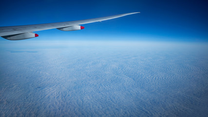 Wall Mural - Close up of window with airplane wing. Beautiful cloudscape with clear blue sky.