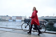 © Westend61 - Denmark, Copenhagen, happy woman pushing bicycle at city harbor in rainy weather