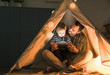 © Westend61 - Father and son sharing a tablet in a dark tent at home