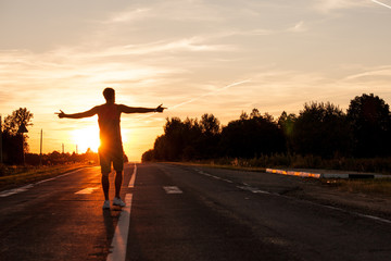 Portrait of happy man walking on a free road or highway with raised hands during lovely sunset