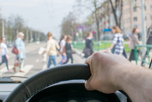 View From The Car, The Man's Hand On The Steering Wheel Of The Car, Located Opposite The Pedestrian Crossing And Pedestrians Crossing The Road