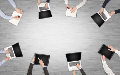 Group of people with devices in hands having desk discussion and making reports together on laptop, tablet, notebook
