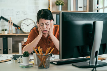 asian woman architect engineer covering ears ignoring annoying loud noise plugs ears to avoid hearing sound. Noisy music problem. frowning upset female designer sick tired hand on face