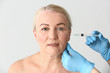 © Pixel-Shot - Mature woman receiving injection in face on light background