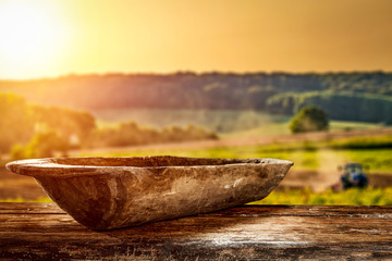 Wall Mural - A wooden old destroyed bowl with space for your decoration. A large wooden table. Sunset in the countryside. Tractor cultivating the field. Summer time.