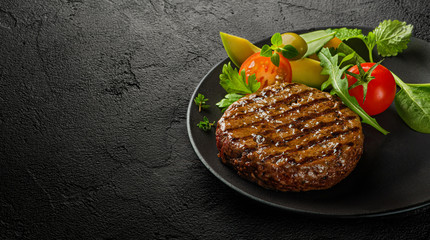 Juicy grilled burger cutlet with salad leaves on dark slate background