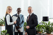 © LIGHTFIELD STUDIOS - selective focus of cheerful businessmen and businesswoman standing in office