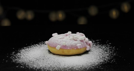 Tasty fresh donut lay on black surface with icing sugar powder