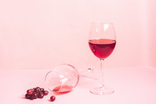 A Glass Of Red Wine On The Table Is Turned Upside Down And A Bunch Of Grapes On Gentle Pink Background. Selective Focus.