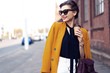 © opolja - Portrait fashion woman in sunglasses walking on street . She wears yellow jacket, smiling to side.