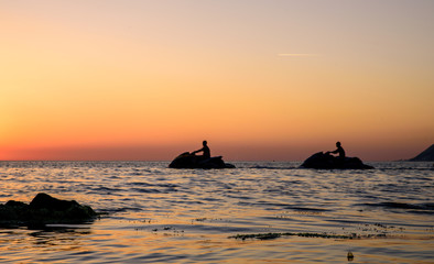 Two silhouettes of aquabike are moving in the ocean at sunset