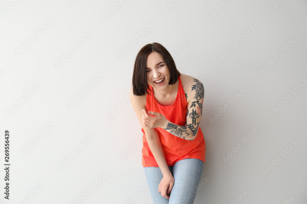 Stylish tattooed woman on light background