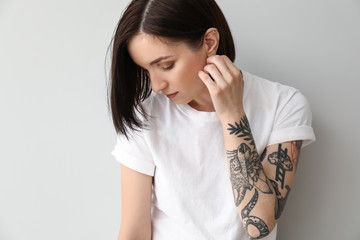 Wall Mural - Stylish tattooed woman on light background