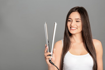 Wall Mural - Young woman with modern hair iron on grey background, space for text