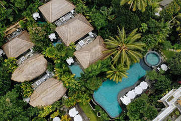 Aerial view of luxury hotel with straw roof villas and pools in tropical jungle and palm trees. Luxurious villa, pavilion in forest, Ubud, Bali