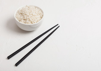 White bowl with boiled organic basmati jasmine rice with black chopsticks on white background. Space for text