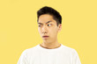 © master1305 - Korean young man's half-length portrait on yellow studio background. Male model in white shirt. Doubts, uncertainly, thoughtful, looking serious. Concept of human emotions, facial expression.
