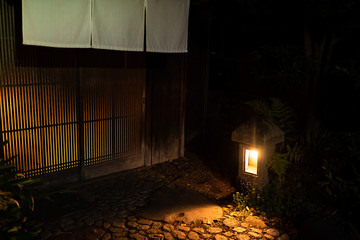 Kyoto, Japan colorful empty street garden in Gion district at night with illuminated golden yellow stone path and wooden wall with curtains