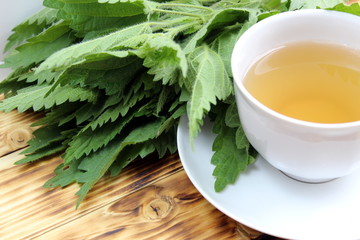 Wall Mural - Cup of tea against the background of green juicy nettle