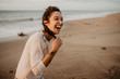 © REMEDIOS PUERTA/ADDICTIVE STOCK - Young lady in casual outfit touching braid and laughing out loud while standing on sandy seashore
