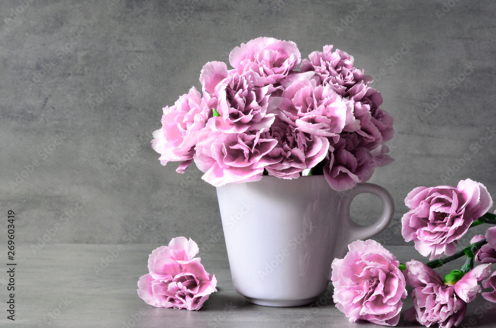 Pink carnation flowers in cup on grey background. - obrazy, fototapety, plakaty 