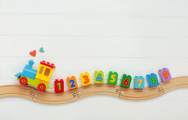 Wall Mural - Kids toy train with numbers on railway on white wooden background with copy space