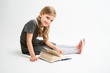 © briagin - Little girl photographed against white background wearing school uniform dress isolated sitting with open book