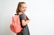 Little girl photographed against white background wearing school uniform dress isolated holding a coral backpack on both shoulders